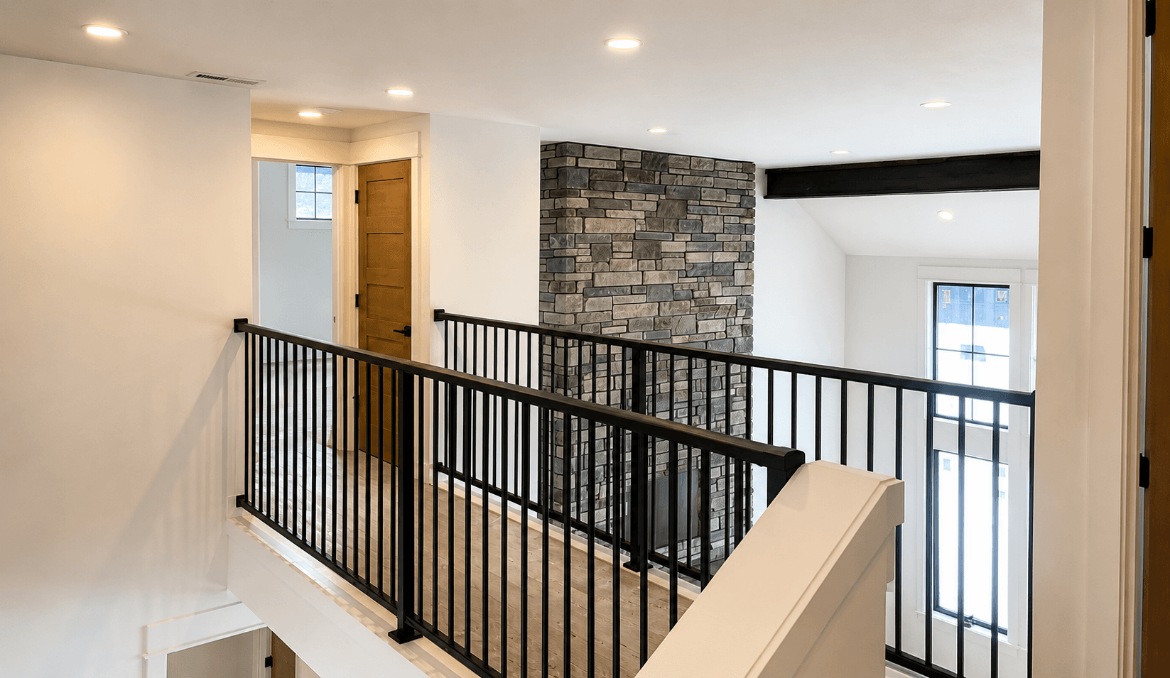 Black aluminum railing along an interior landing beside a stone chimney