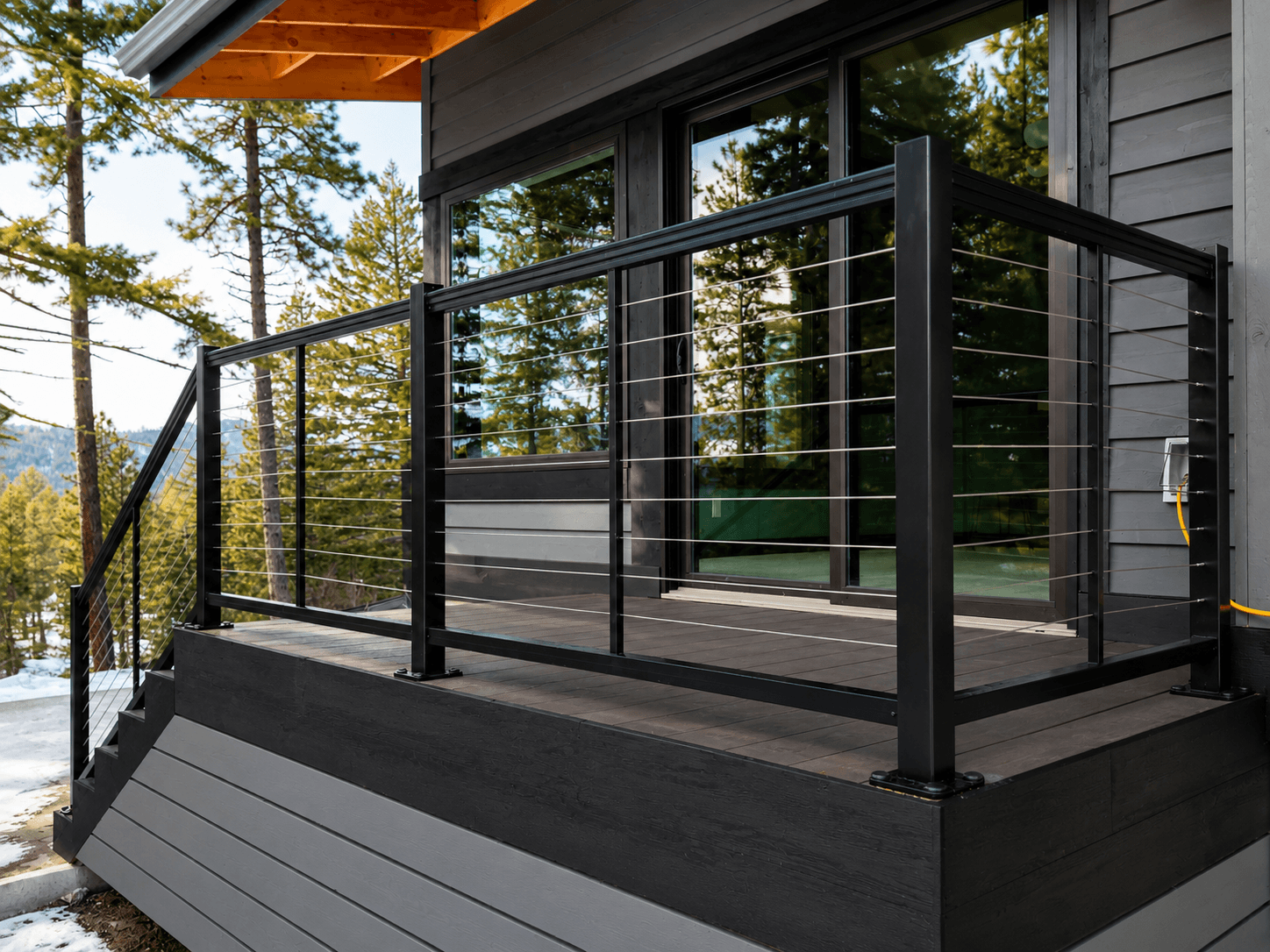 Black-framed stainless cable railing on a composite deck and stairs at a mountain cabin