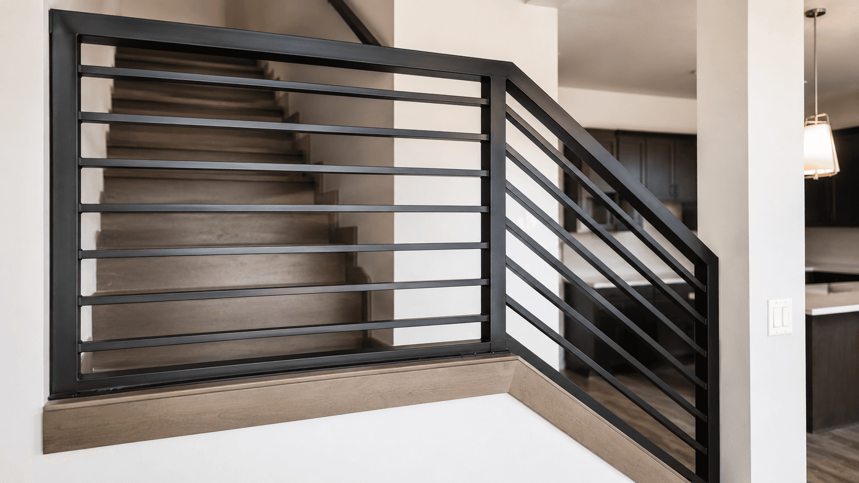 Custom black horizontal-bar metal railing on a stair landing overlooking the staircase and kitchen
